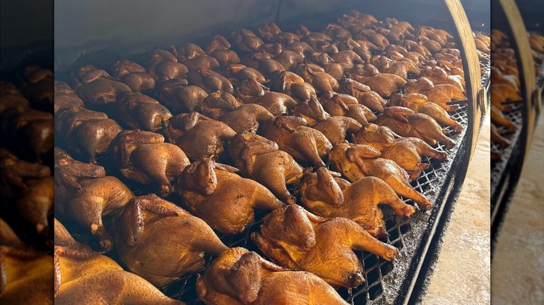 A large smoker grate with dozens of whole chickens cooking on it
