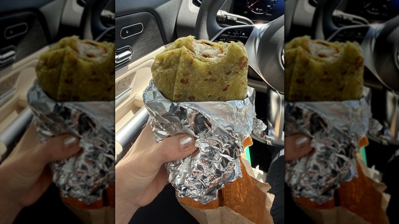 Close-up of someone eating a foil-wrapped Cabo Bob's fish burrito in their car