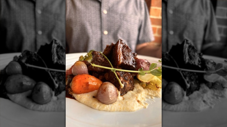 Roasted lamb on a white plate over polenta with whole root vegetables