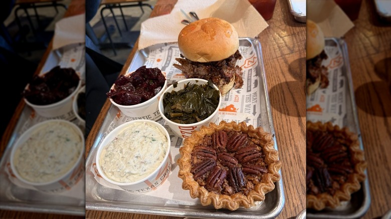 A metal tray with a ZZQ's pulled pork sandwich, beets, collard greens, potato salad, and a mini pecan pie
