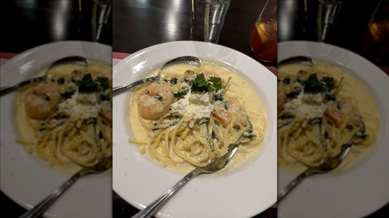 Shrimp scampi on a white plate with a spoon and a knife