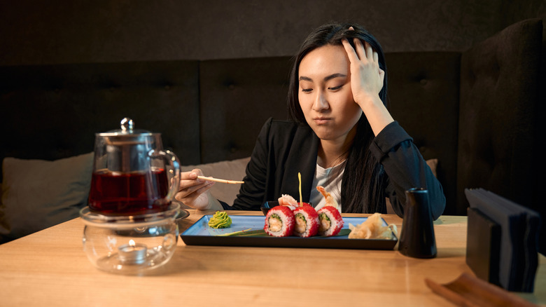 Woman looks grumpy while eating sushi.