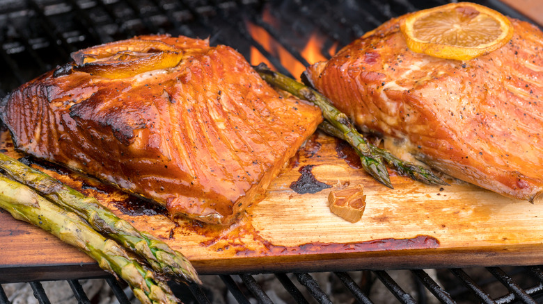 Two pieces of salmon and asparagus cooking on a cedar plank over a grill