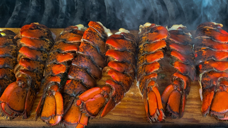 Red lobster tails grilling on a cedar board with smoke rising
