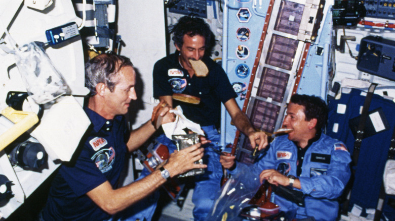 A team of astronauts eating a meal while on board the Space Shuttle Discovery