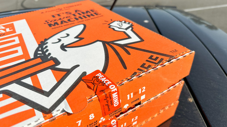 A stack of orange Little Caesars pizza boxes with the Caesar-themed mascot