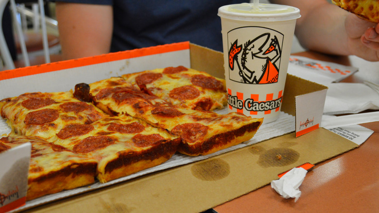 A pepperoni Little Caesars deep dish pizza in a box with a soda cup featuring their mascot