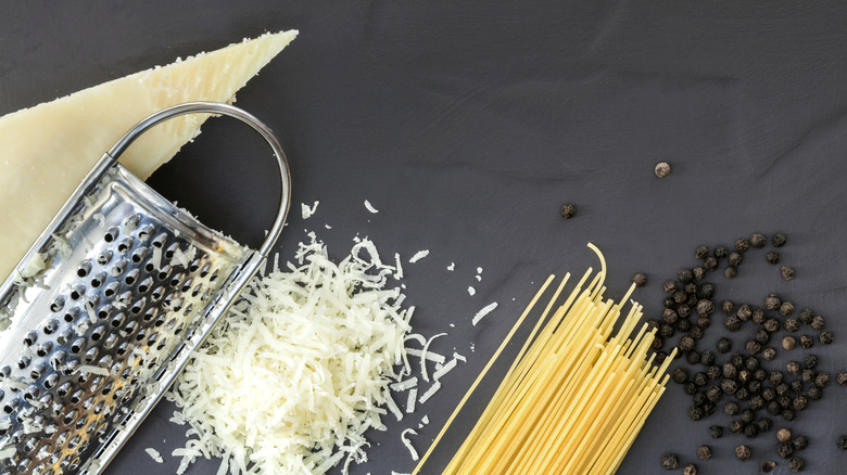 Hard grated cheese, grater, dry pasta, peppercorns on black