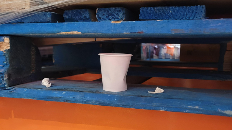 A paper cup and debris between the boards of a wooden pallet at Costco