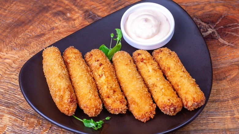 Fried mozzarella sticks on a black plate with dipping sauce.