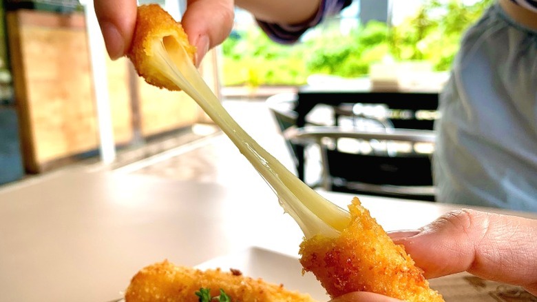 A person demonstrating a cheese stretch with a mozzarella stick.