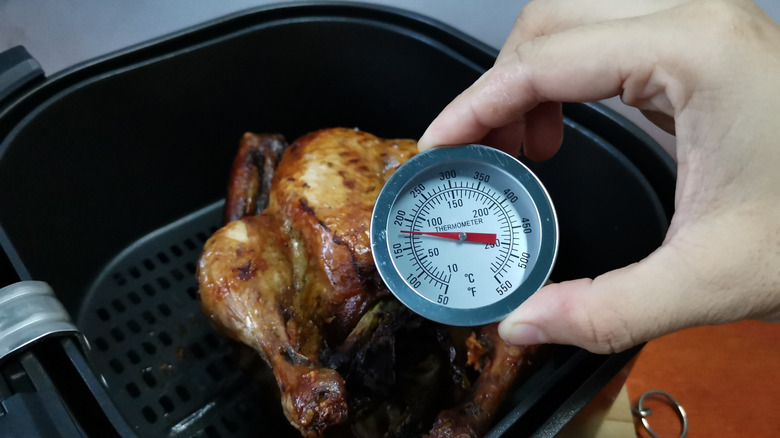 Someone checking the internal temperature of a chicken with a thermometer.