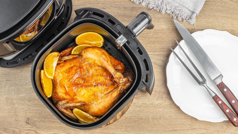 Air fried whole chicken with lemon wedges in an air fryer basket.
