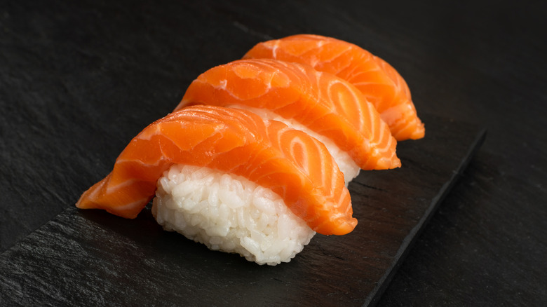Three pieces of salmon over rice on a black serving platter