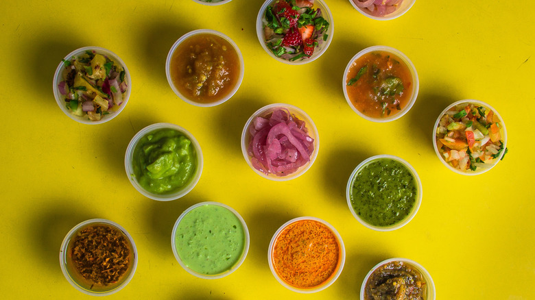 Top view of assorted Mexican salsas in plastic condiment cups on yellow background