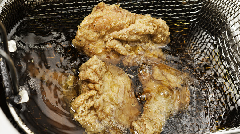 aerial view of three pieces of chicken in a basket frying in oil