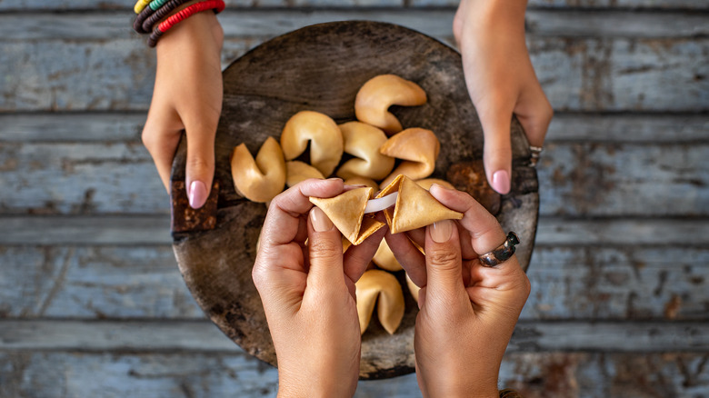 Two sets of hands and a bowl full of fortune cookies