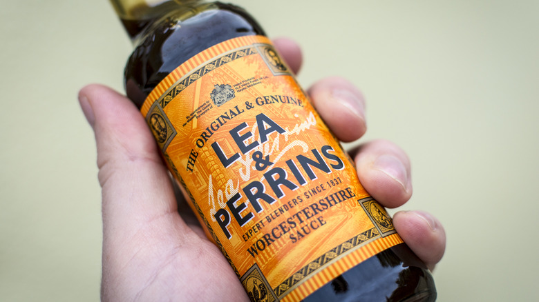 A closeup of a hand holding a bottle of Lea & Perrins Worcestershire sauce