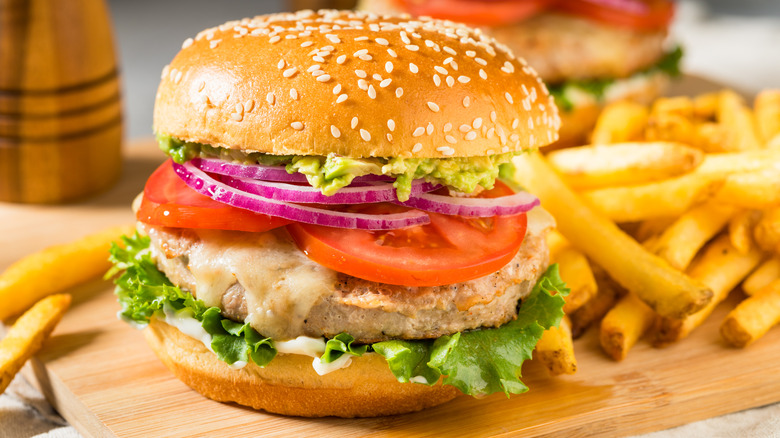 A turkey burger with lettuce, onion, and tomato near french fries on a wooden surface