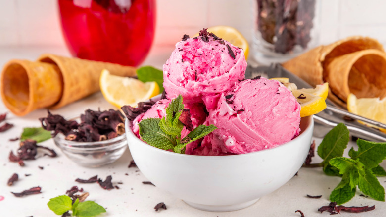 Pink ice cream in white bowl with mint sprigs and lemon slices