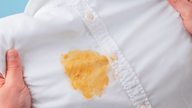 Dirty yellow stain on a white shirt, hands showing for visual evaluation of stain