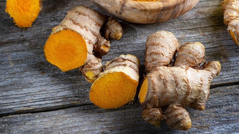 Curcuma longa, powder, rhizomes and tea, bright orange. Powder and root form in a wooden bowl