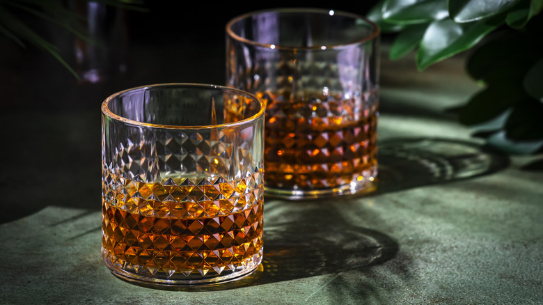 Two textured glass tumblers containing whisky on a green cloth