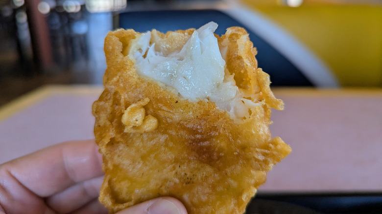 Hand holding battered fried fish filet partly ripped open.