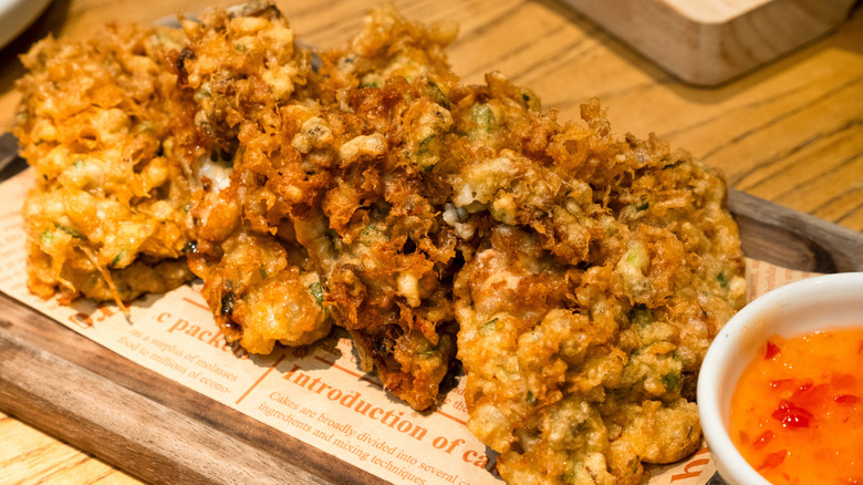 Fried oysters sit on a wooden plate with a bowl of sweet chili sauce for dipping