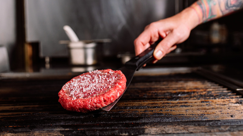 A chef flips a salted burger patty on a grill