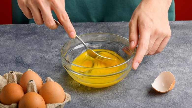 Person whisking eggs in a glass bowl with a fork
