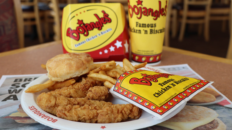 Bojangles fried chicken tenders with biscuit and fries on a paper plate with box and drink in background
