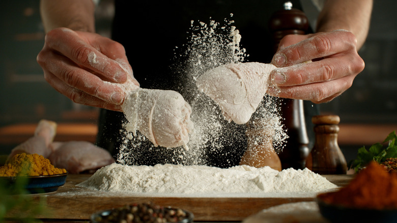 Person dredging chicken legs with one in each hand and flour flying