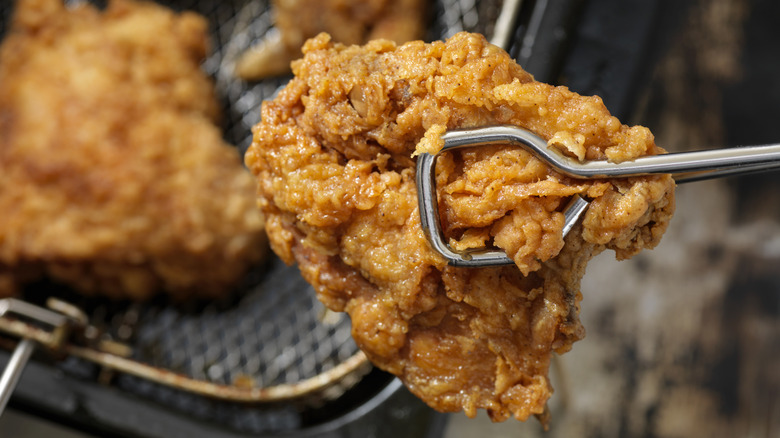 Close up of fried chicken being held up with tongs fresh out of the fryer