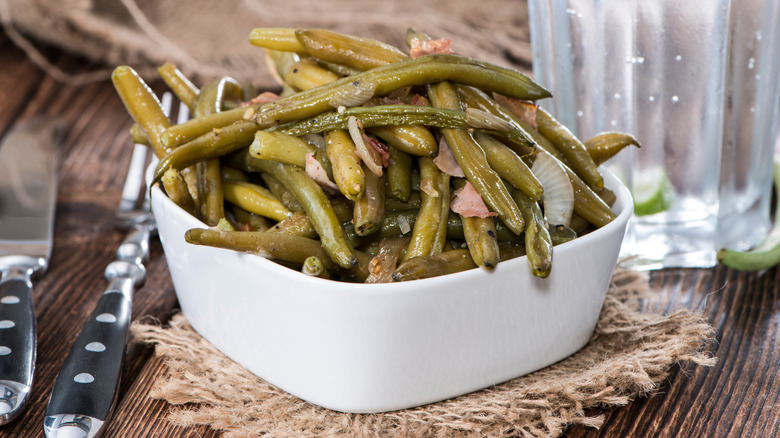 White dish filled with green beans with bacon