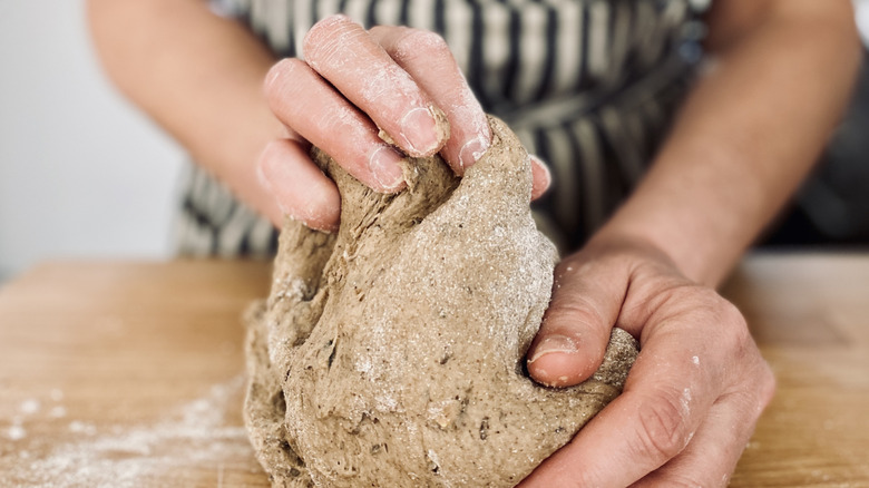 Hands kneading a rye-based bread dough with the baker's striped apron in the background in soft focus