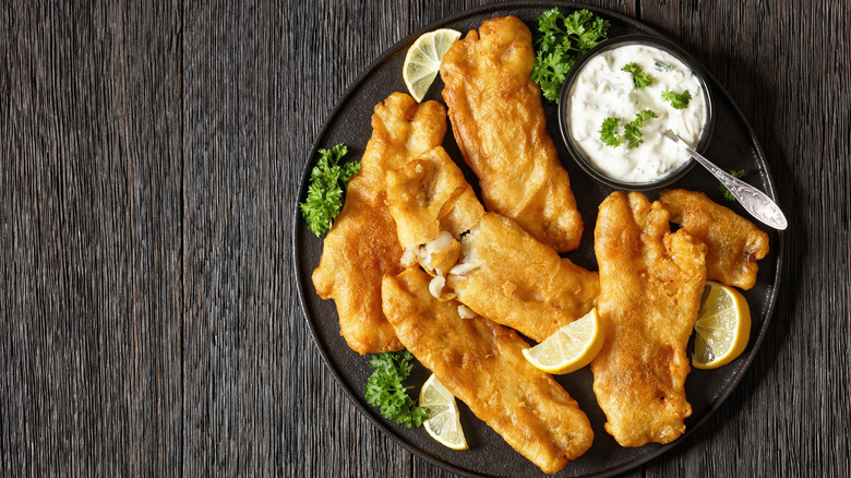 Deep-fried fish fillets with lemon and tartar sauce on a black plate
