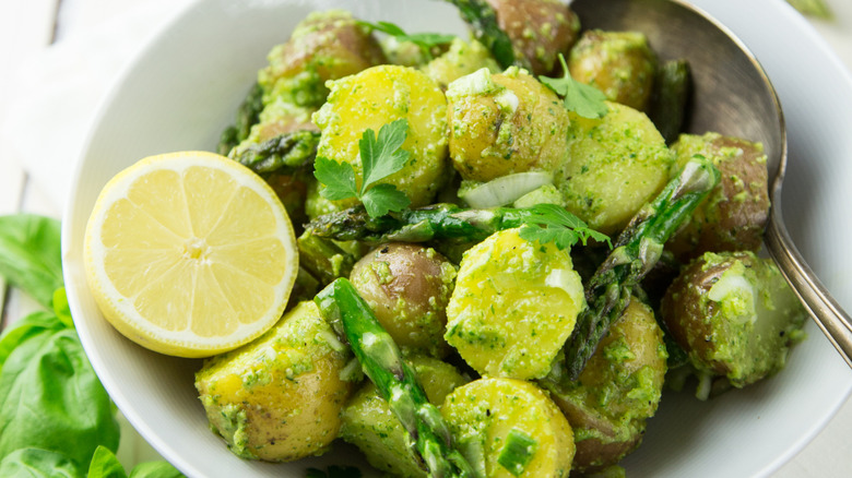 pesto potato salad with lemon wedge in white bowl.