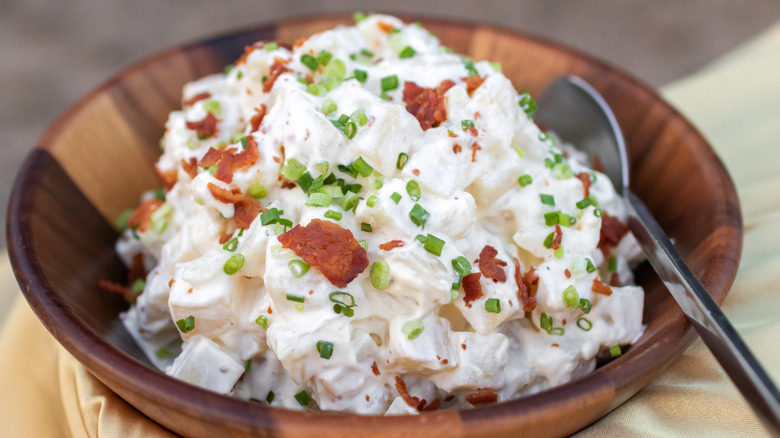 potato salad in wooden bowl topped with chives and bacon bits.