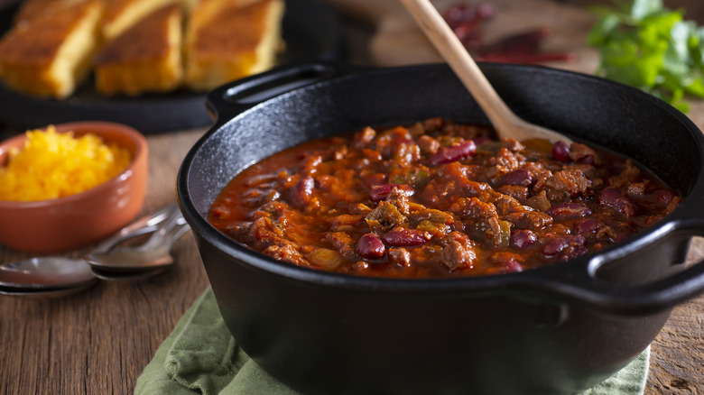 Cooked chili in a black Dutch oven with a wooden spoon in it