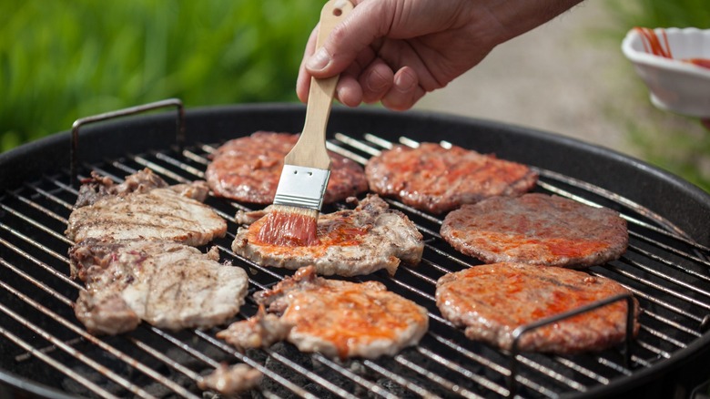 Brushing sauce onto burger patties on a grill