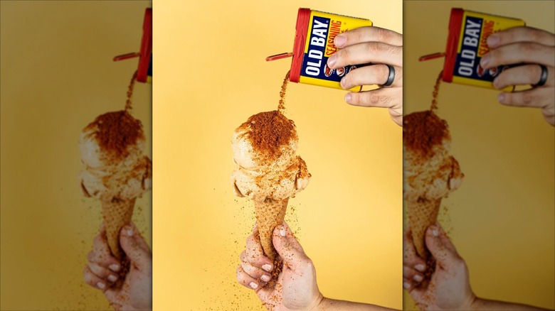 A hand pouring Old Bay seasoning on an ice cream cone