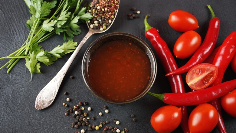 Top view of hot sauce in a small bowl flanked by herbs, peppercorns, and chiles.
