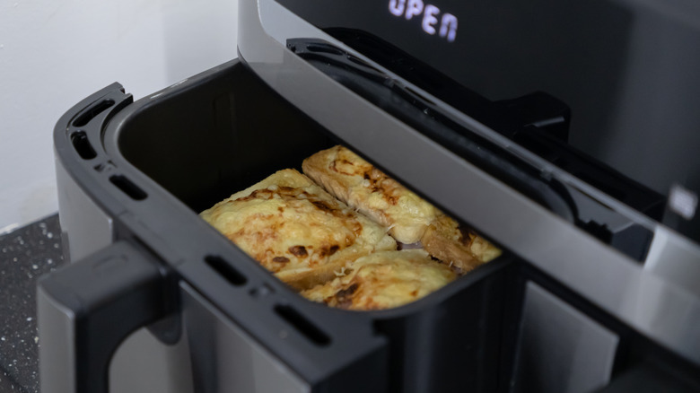 Slices of bread topped with cheese in a slightly open air fryer