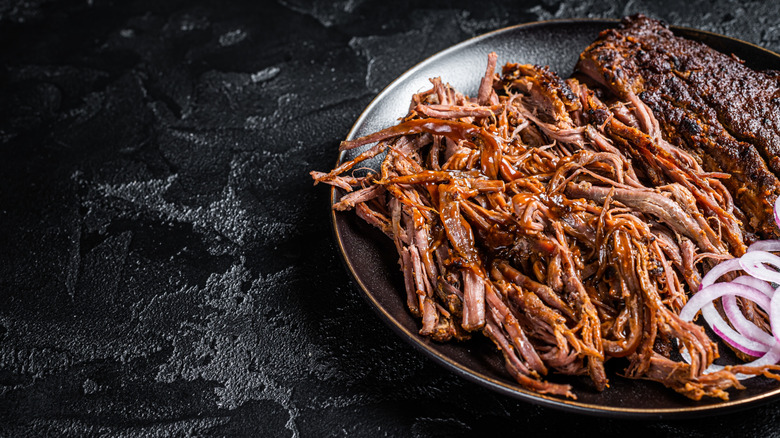 Shredded meat with sauce and onions on dark plate