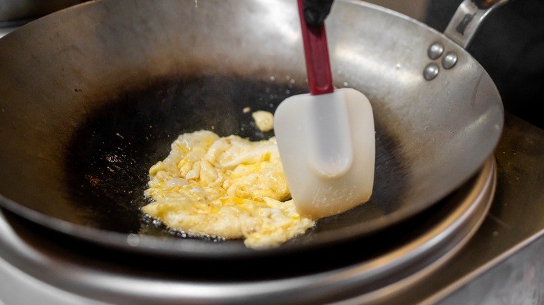 Person using spatula to make scrambled eggs in stainless steel pan