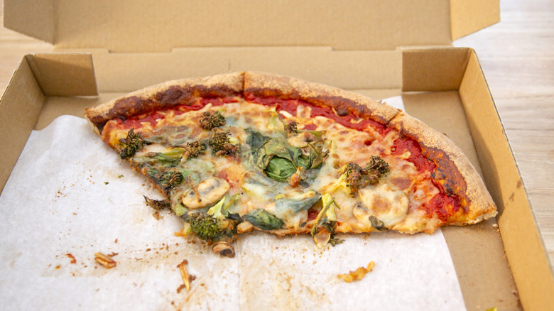 Leftover pizza with broccoli and basil in cardboard box