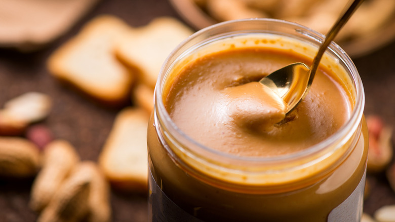 An open jar of creamy peanut butter with a spoon in it.