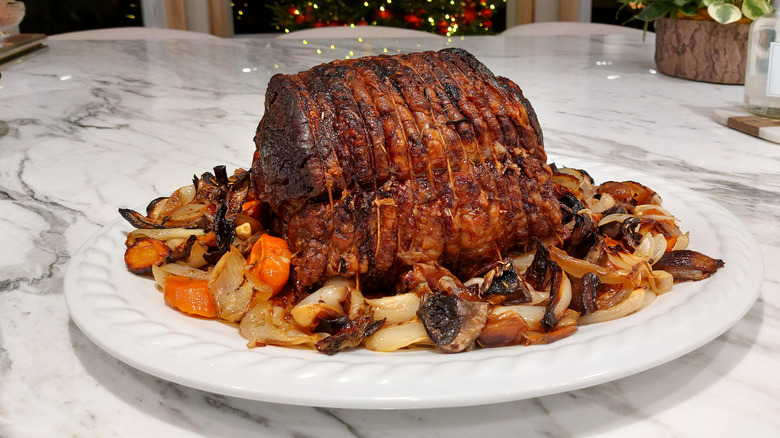 Roasted prime rib on a white platter surrounded by vegetables on a marble table
