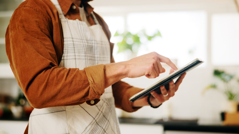 Person reading recipe on an electronic tablet wearing apron